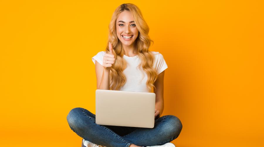 一个女人微笑着竖起大拇指，坐在黄色背景下的笔记本电脑旁