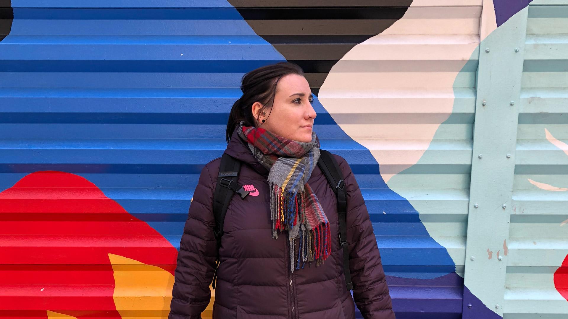 安吉拉·罗奇站在纽约五颜六色的街头艺术前. It&现在是十一月，她穿着羽绒服，围着围巾.
